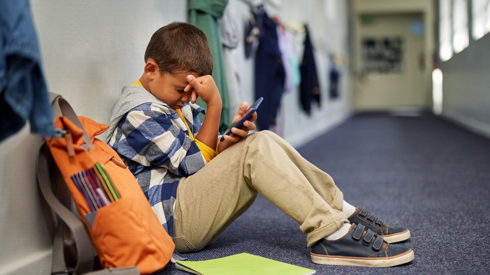 School boy being cyberbullied looking at the screen of his phone with a sad expression