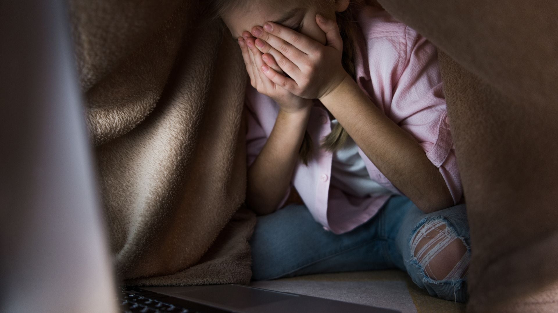 Child on her bed upset and sad because of cyberbullying