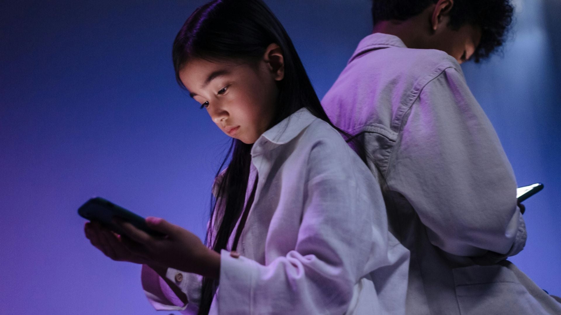 Young girl on her phone trading items in her favorite online game, and older boy back-to-back with the girl represents the person she is trading with